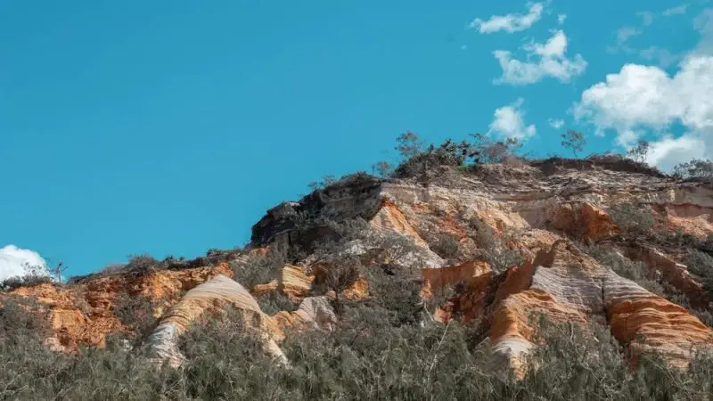 Vivid multi-coloured rock cliffs with scattered greenery shine beneath a clear blue sky on your Kgari 3 Day Getaway adventure.