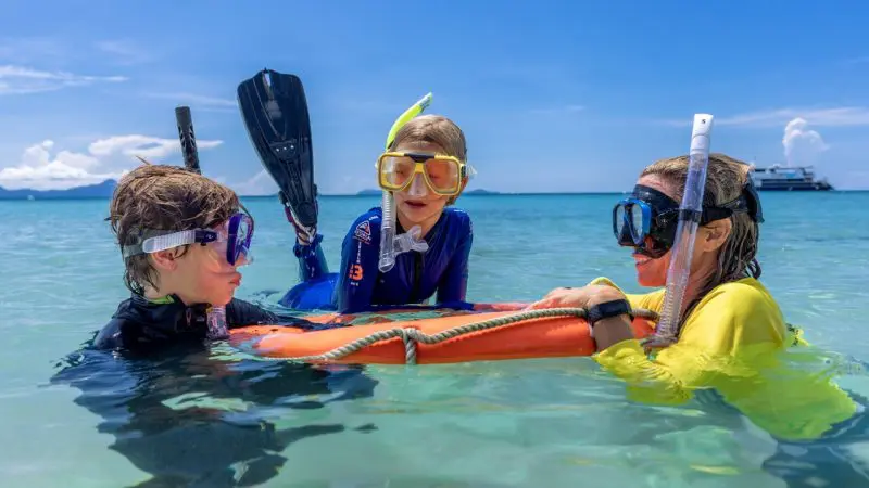 Children snorkelling in crystal-clear blue waters with an orange float ring on a Frankland Island Express Tour, Great Barrier Reef.