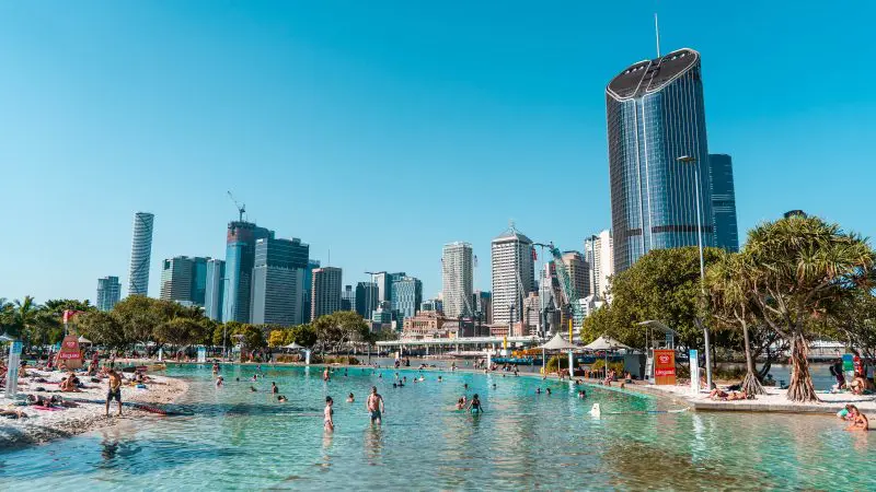 Swimmers enjoy a crystal-clear lagoon against Melbourne’s iconic skyscraper skyline under sunny blue skies—an unforgettable adventure.