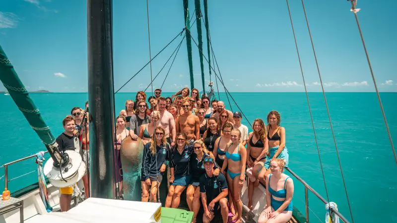 Group of friends in colourful swimwear enjoying a guided sailboat tour on the Ultimate East Coast Sydney to Cairns adventure.