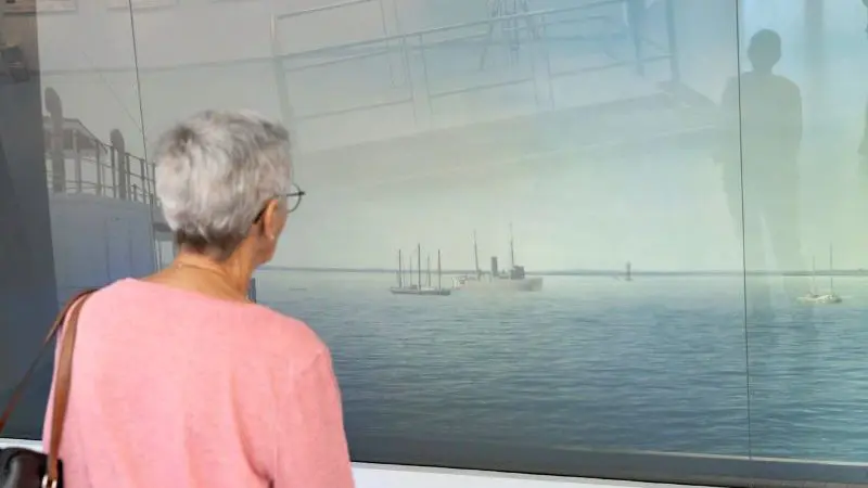 Senior woman with grey hair explores a maritime museum, admiring ship displays, using an RFDS Darwin Aviation Attraction Combo Ticket.