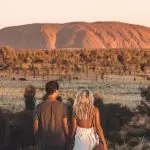 Couple watching sunset over Uluru in the Australian Outback desert during a 2 Day Red Centre Rock Tour from Alice Springs.
