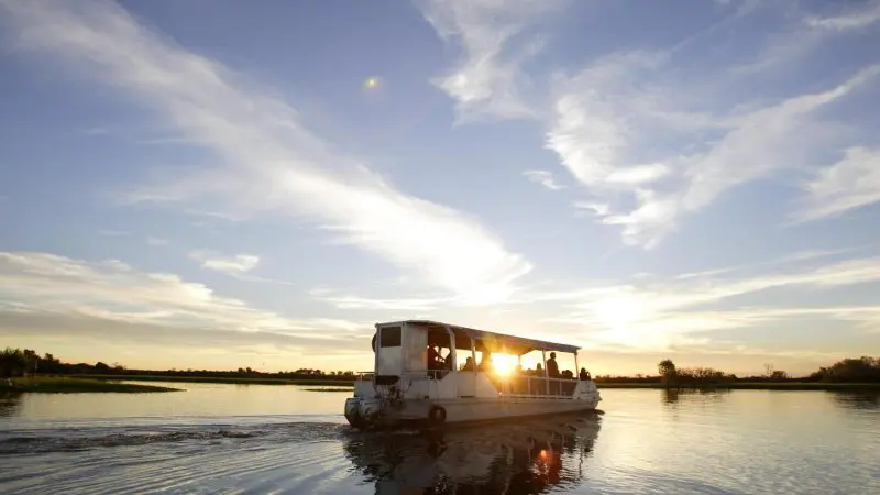 A serene boat glides at sunset on calm waters during a 2 Day Kakadu Outback Retreat Tour from Darwin, with scattered clouds above.
