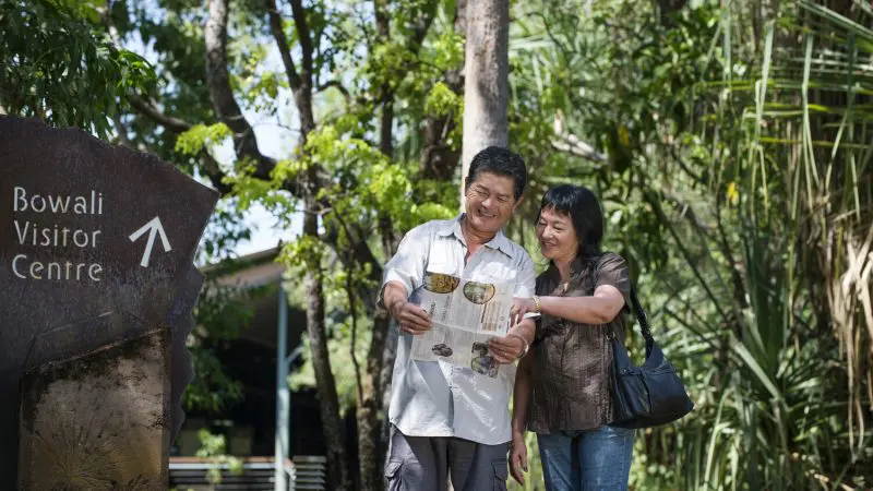 Happy couple study a map by the Bowali Visitor Centre sign during a 2 Day Kakadu Outback Retreat Tour departing from Darwin.