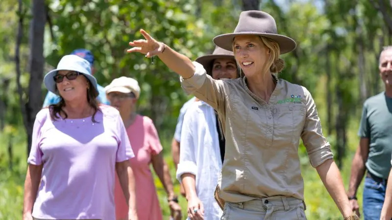 A woman in a hat guides a 5-day Kakadu, Katherine Gorge, and Litchfield 4WD tour from Darwin, set in a lush, sunlit landscape.