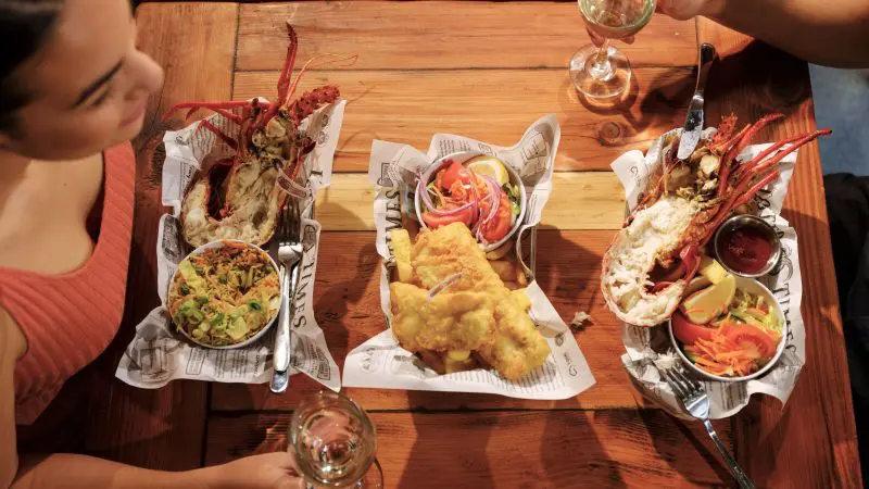 Two travellers savour fresh lobster halves and white wine at a rustic table on the Pinnacles Lobster Lavender Day Tour from Perth.