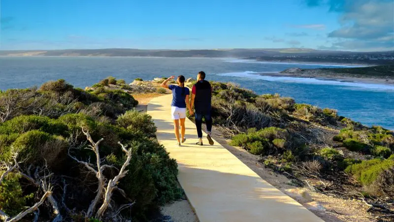Two people hike the scenic coastal trail on the Perth to Monkey Mia 4 Day Loop Tour, stunning ocean views stretching alongside them.