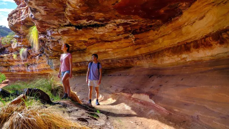 Two hikers explore vibrant, layered rock formations on the scenic 4 Day Perth to Monkey Mia Coastal Loop Return Tour in Western Australia.