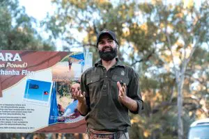 Bearded man sharing insights by the Adnyamathanha Flag during the 7 Day Adelaide to Uluru Adventure tour with Untamed Escapes.