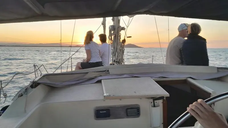 Experience a Townsville Lunchtime Sailing Private Charter at sunset—four guests relax onboard as one expertly steers the yacht.