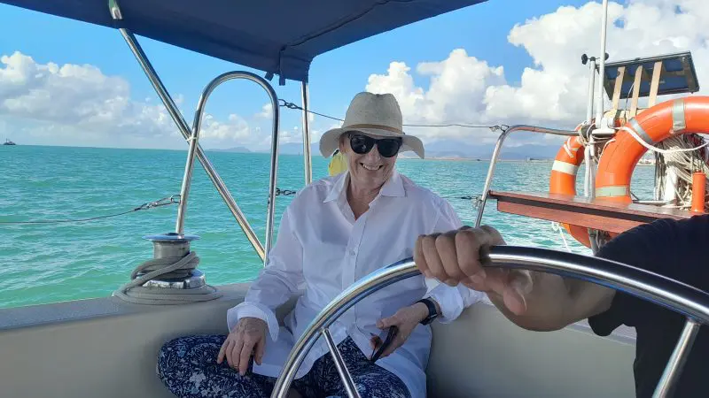 Smiling woman in sunglasses and sunhat enjoys Townsville Lunchtime Sailing Private Charter with vibrant blue sea and sky backdrop.