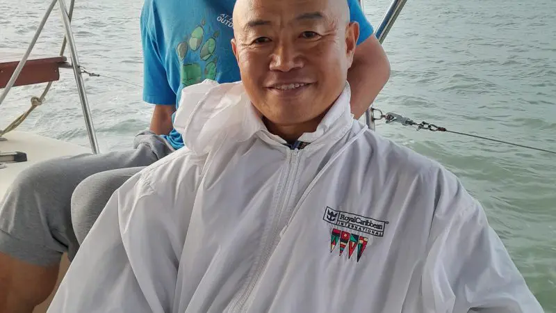 Two men enjoy a Townsville Lunchtime Sailing Private Charter—one seated in white, the other standing in blue shirt and cap, smiling.