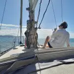 Guest in a crisp white shirt enjoys a refreshing drink aboard a Townsville Lunchtime Sailing Private Charter with scenic blue sea and mountain views.