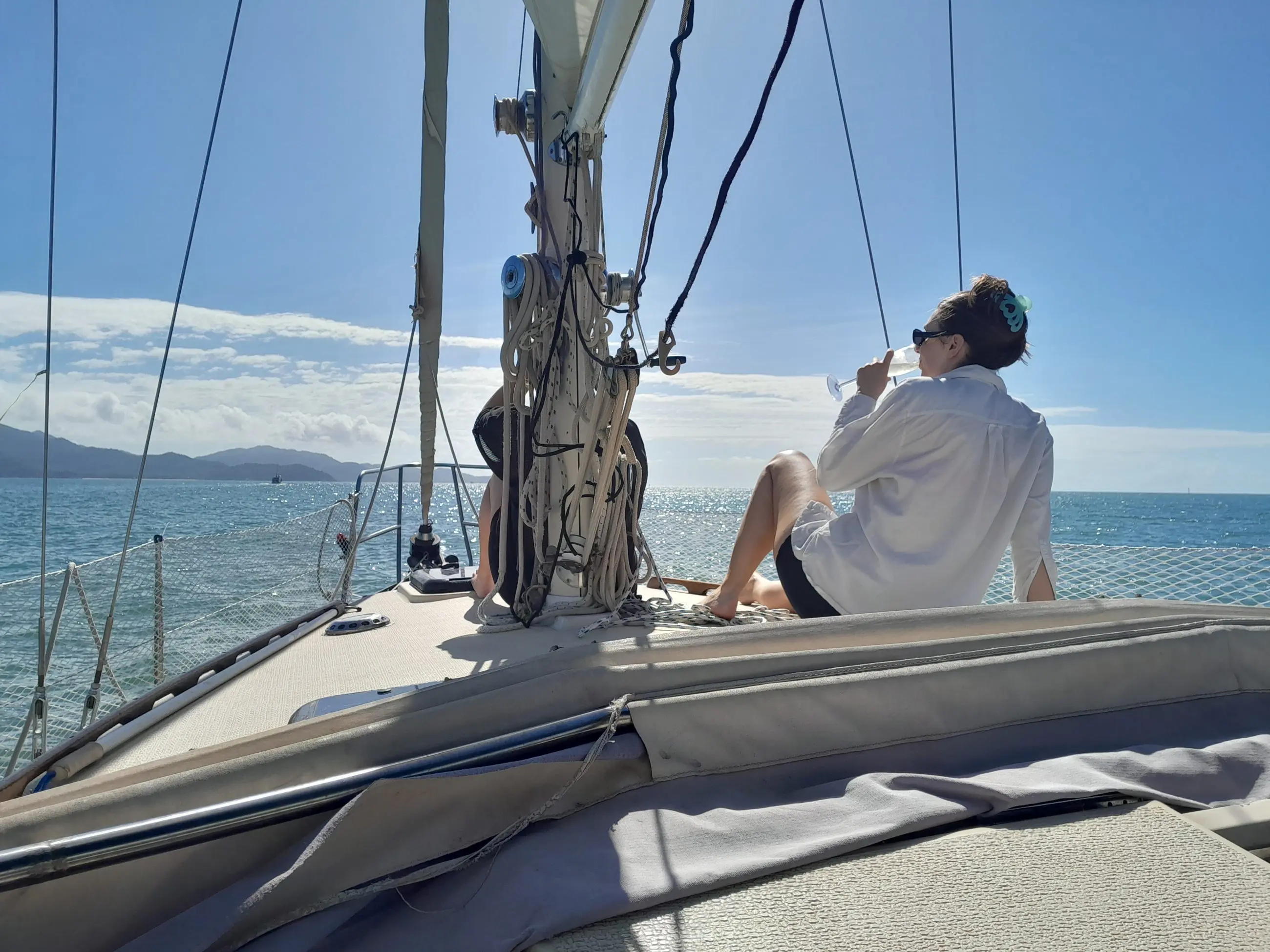 Guest in a crisp white shirt enjoys a refreshing drink aboard a Townsville Lunchtime Sailing Private Charter with scenic blue sea and mountain views.