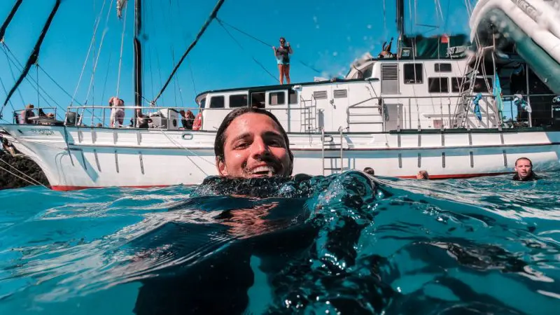 A happy swimmer enjoys crystal-clear Whitsunday waters near New Horizon during a 2 Day 2 Night sailing adventure under sunny skies.