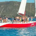Vibrant group in swimwear waves from a striking red sailboat on the Siska 2 Day 1 Night Whitsundays Sailing adventure tour.