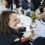 Smiling woman at a sunlit table holding a menu during Colourful Collective’s Hunter Valley wine tour, savouring premium wines.