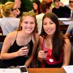Two young women savour wine outdoors at a 1 Day Hunter Valley Wineries Tour from Sydney, surrounded by scenic vineyard views.