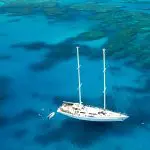 The Summer Jo 2 white sailboat anchored in crystal-clear Whitsunday waters with swimmers exploring vibrant coral reefs below.