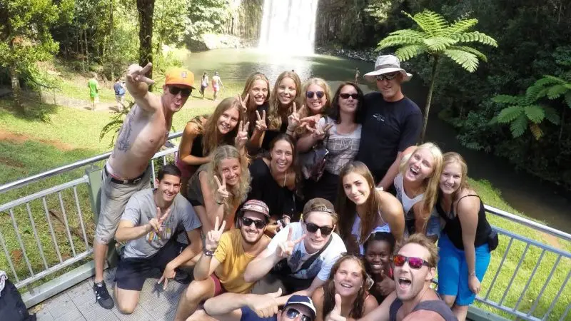 Tourists smiling and posing for a group photo by a stunning waterfall on the Cape Tribulation Atherton Tablelands adventure tour.