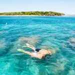 Two snorkellers and a glass-bottomed boat at Green Island above vibrant coral reef, gliding over crystal-clear blue waters in Cairns, Australia.