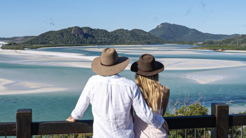 A couple wearing hats overlooking a swirling sands formation at Hill inlet viewpoint