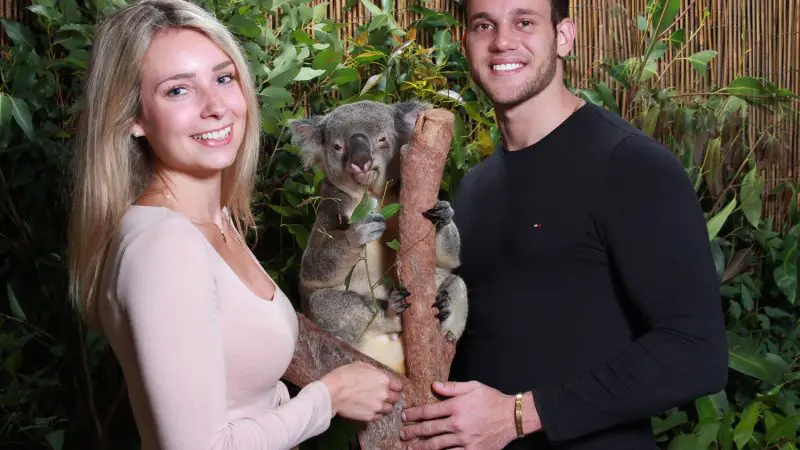 Happy couple pose with a koala amid lush rainforest on their Kuranda Scenic Railway Deluxe tour, capturing an unforgettable adventure.