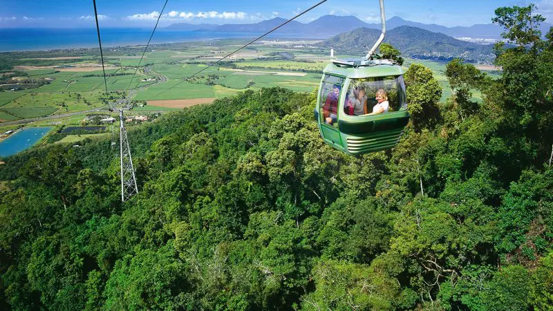 Luxury Grand Kuranda cable car soars over vibrant rainforest, offering guests unrivalled panoramic views of majestic mountains and fields.