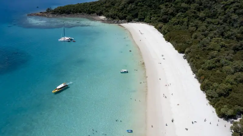Stunning aerial view of Whitehaven Beach’s turquoise waters, boats, swimmers, and lush forest—top spot for snorkelling enthusiasts.