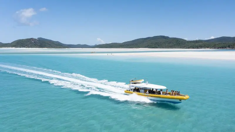 Yellow speedboat glides by Whitehaven Beach, lush Whitsunday hills and top Coral Reef snorkelling sites visible in turquoise waters.