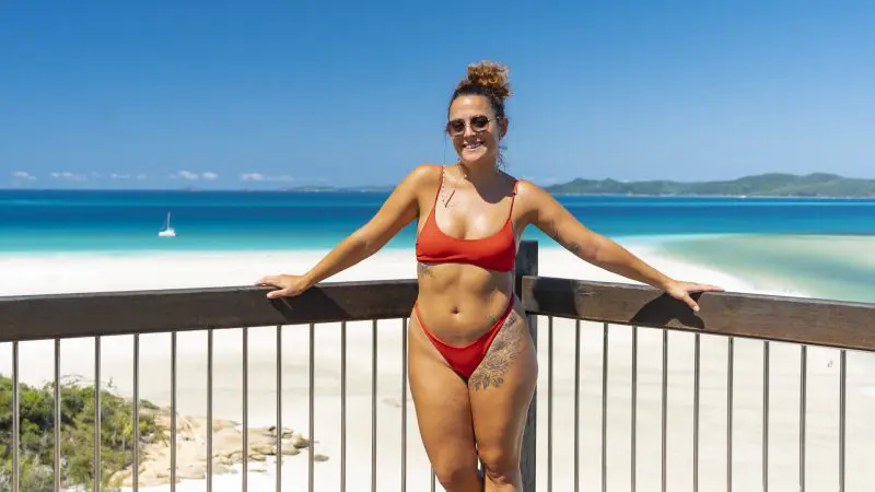 Woman in red bikini stands on deck, admiring Big Fury Whitsundays’ stunning Whitehaven Beach and crystal-clear coral reef waters.
