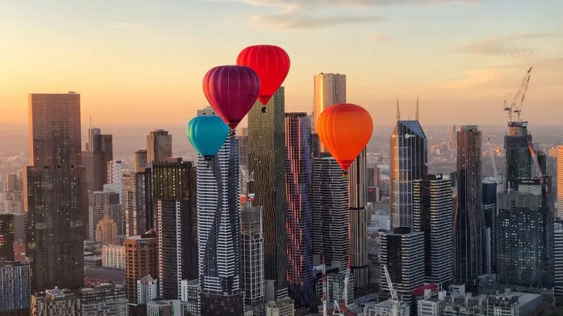 Vibrant hot air balloons soar above Melbourne skyline at golden sunset during a breathtaking 1-hour sunrise balloon flight experience.