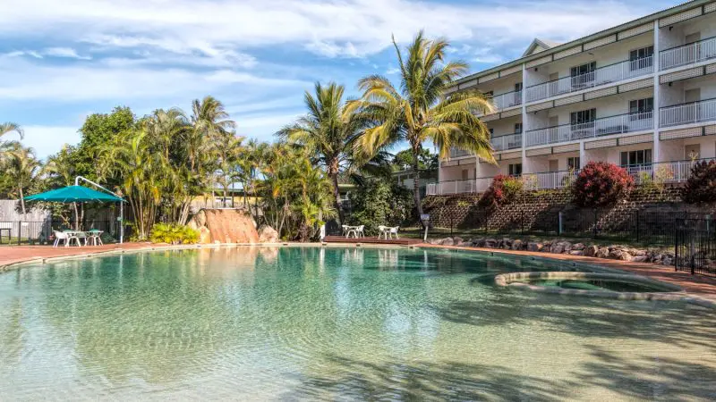 Luxurious outdoor pool surrounded by palm trees, loungers, and a modern hotel—ideal relaxation after your Kgari 2 Day Tour ex Hervey Bay.