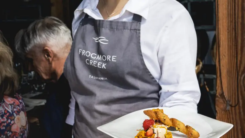 A cheerful waiter in a Frogmore Creek apron presents pudding—a delightful finale to your Coal River Valley Wine and Gin Safaris tour.