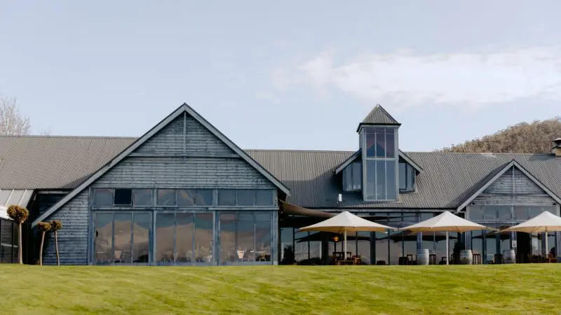 Modern rustic venue with expansive windows, outdoor patio seating, and shaded parasols—perfect for Coal River Valley Wine & Gin Safaris tours.