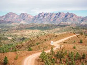 Scenic dirt road with white caravan on 6-Day Eyre Peninsula Flinders Ranges Adventure Tour headed towards dramatic rocky mountain ranges.