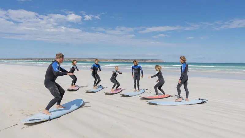 Adventurers in wetsuits surf on a scenic sandy beach during the 6 Day Eyre Peninsula Flinders Ranges Adventure Tour in Australia.