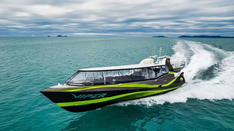 VIPER, a striking black and green speedboat, powers through the Outer Great Barrier Reef Tour beneath dramatic cloudy skies.