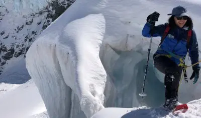 Adventurer in winter gear hiking snowy terrain by massive ice formation on Mt Cook tour, sunlight glistening on pristine snow.