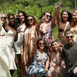 Stylish friends toast with wine glasses at a Yarra Valley winery tour, smiling and enjoying a sunny day in scenic vineyard surroundings.