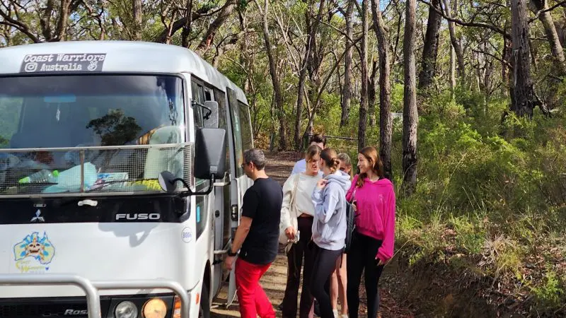 Travellers queue to board a white minibus for a Blue Mountains Day Tour, featuring scenic waterfall walks and stunning views.