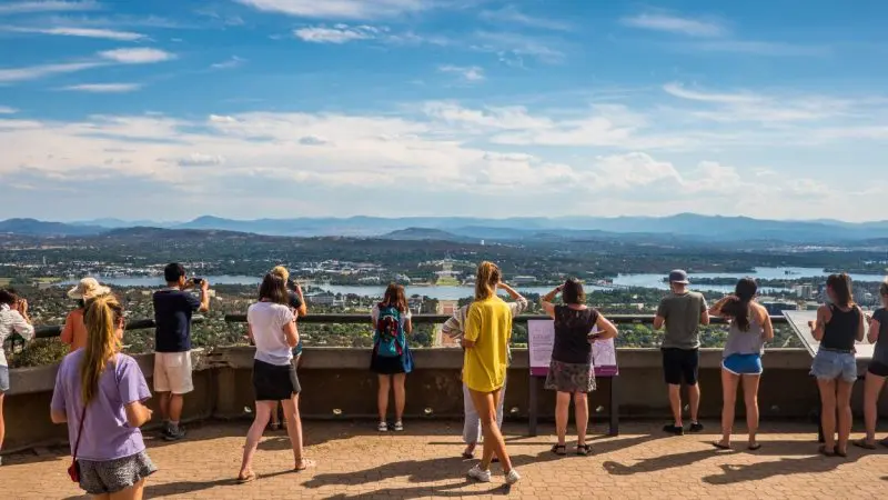 Travellers enjoy a panoramic Canberra Day Trip from Sydney, taking in stunning cityscapes, mountain vistas, and sparkling lakes under clear blue skies.