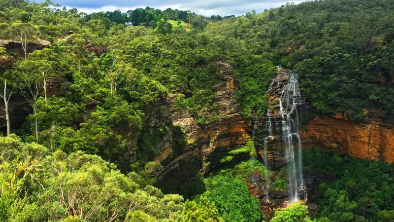 Majestic waterfall plunges over striking orange cliffs, a must-see highlight of the Blue Mountains All-Inclusive Signature Day Tour.