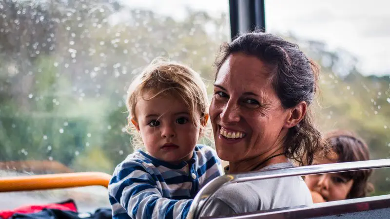 Smiling woman with her children aboard the Explorer Bus Pass, enjoying a rainy Hop On Hop Off tour and memorable family sightseeing.
