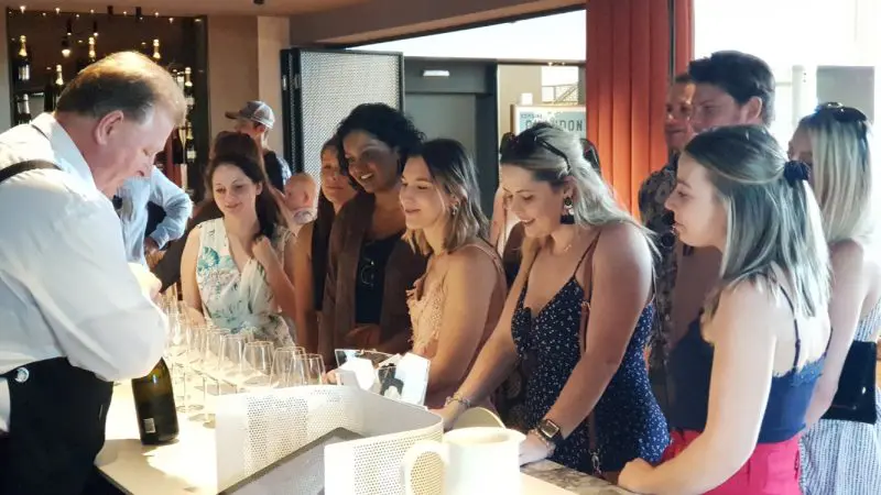 Guests savour a Yarra Valley wine tasting, watching an expert pour premium wines into glasses at a stylish bar during the event.