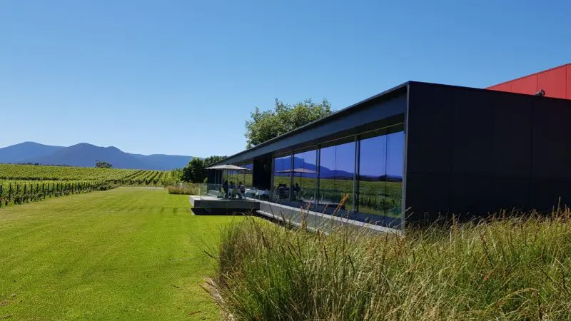 Contemporary winery with expansive glass windows offers panoramic views over lush Yarra Valley vineyards, ideal for top wine tasting.