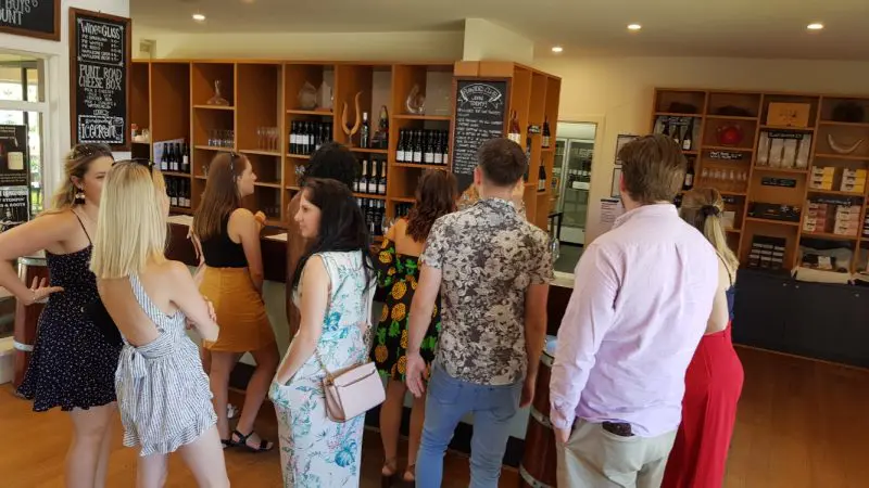 Visitors savour premium Yarra Valley wine tasting at a stylish bar, surrounded by illuminated shelves filled with assorted wine bottles.