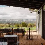 Experience stunning views of McLaren Vale South from an outdoor patio with sleek black metal tables, chairs, and Hop On Hop Off Tour allure.