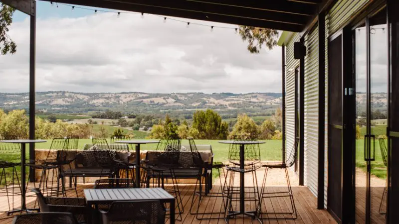 Experience stunning views of McLaren Vale South from an outdoor patio with sleek black metal tables, chairs, and Hop On Hop Off Tour allure.