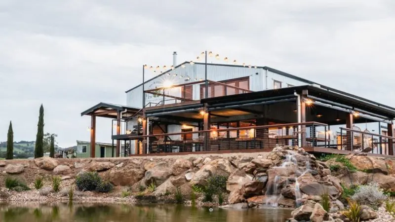 Stunning modern farmhouse with expansive windows, glowing fairy lights, scenic rocks and tranquil pond on McLaren Vale South tour route.